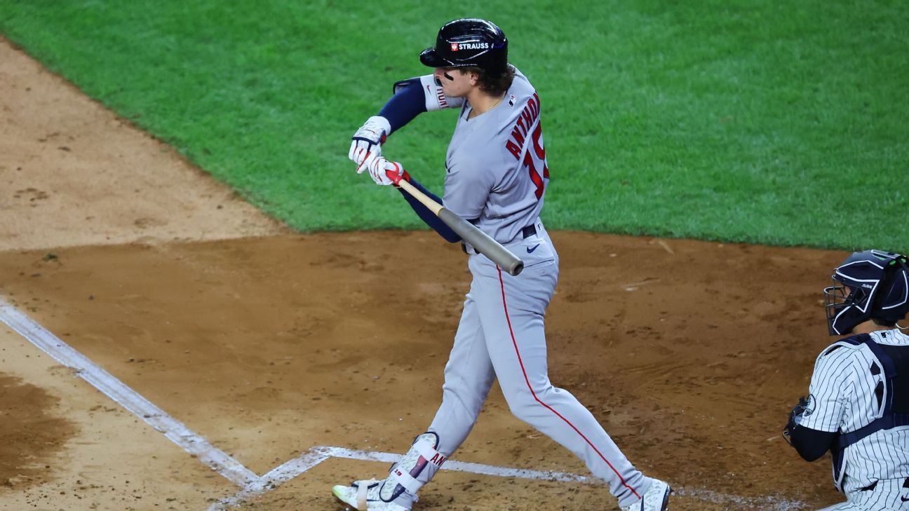 A Red Sox batter swings as a Yankees catcher crouches behind him at home plate.