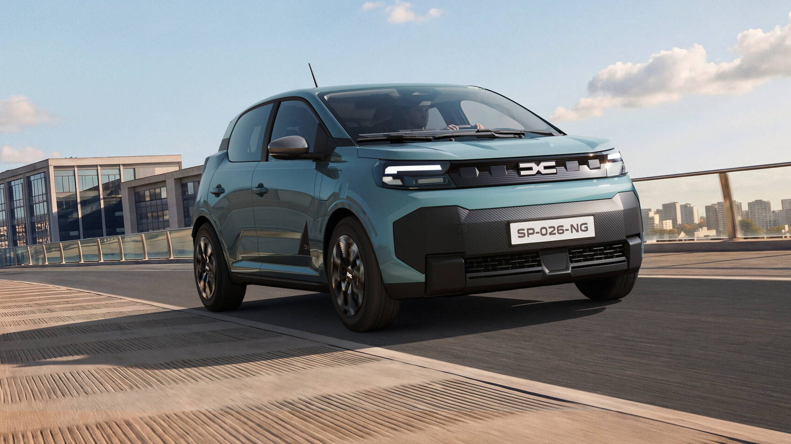 Blue Dacia Spring electric car driving across a bridge beneath a partly cloudy sky.