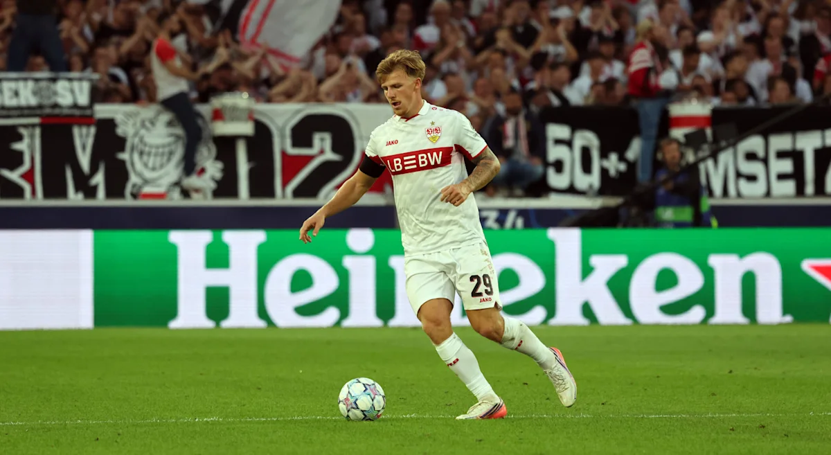 Footballer in white kit dribbles a ball across a soccer pitch during a match