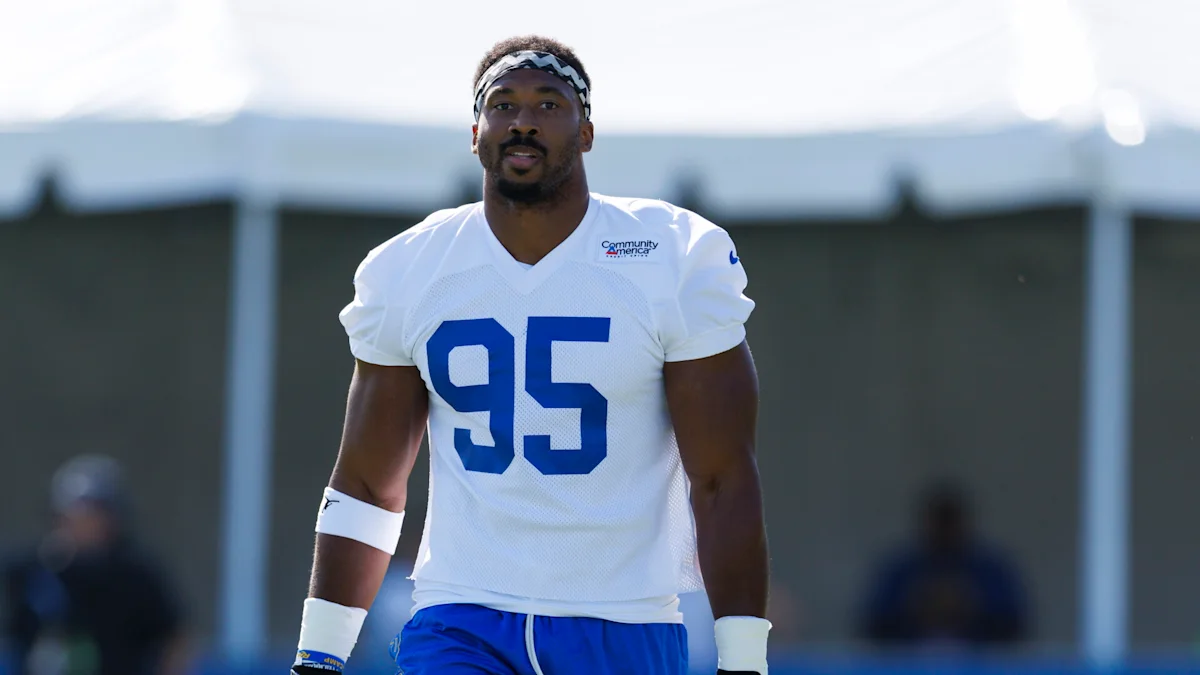 Football player wearing a white number 95 jersey and blue pants stands on a practice field.