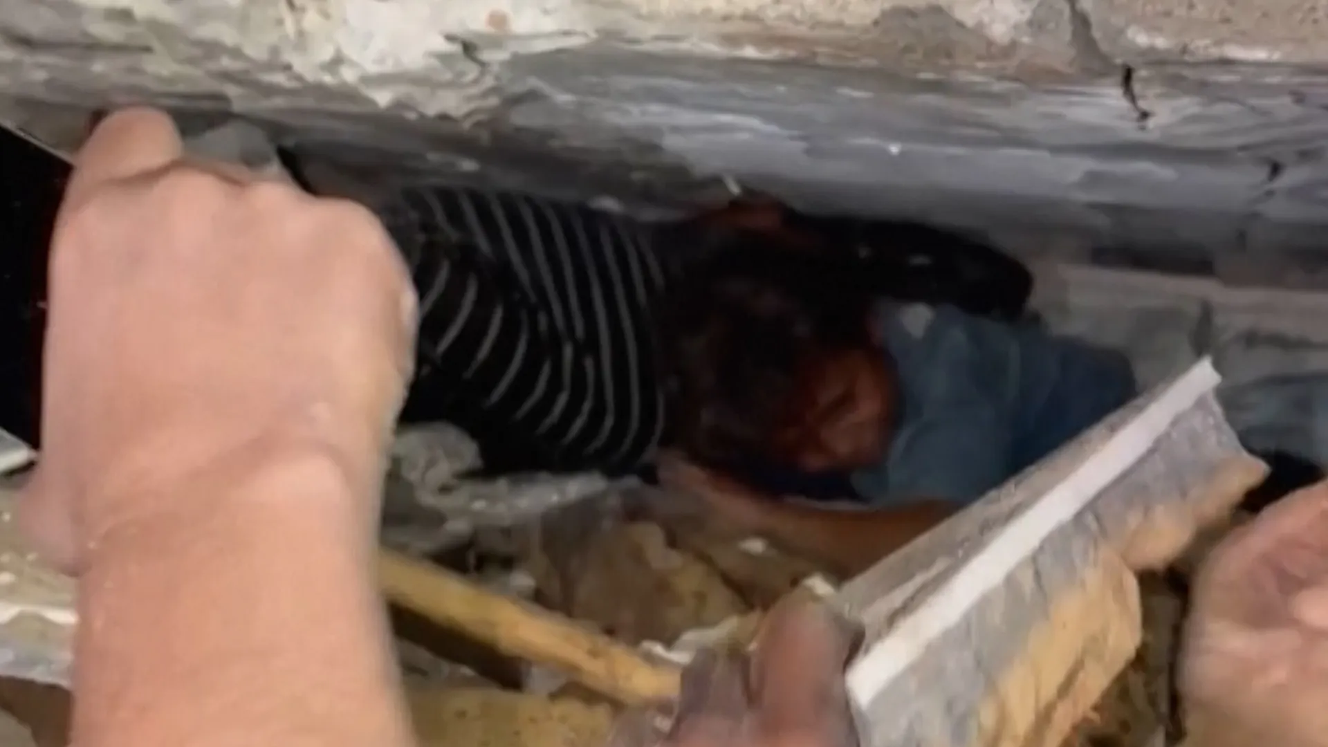 Rescue workers uncover a person trapped beneath concrete rubble using hand tools.