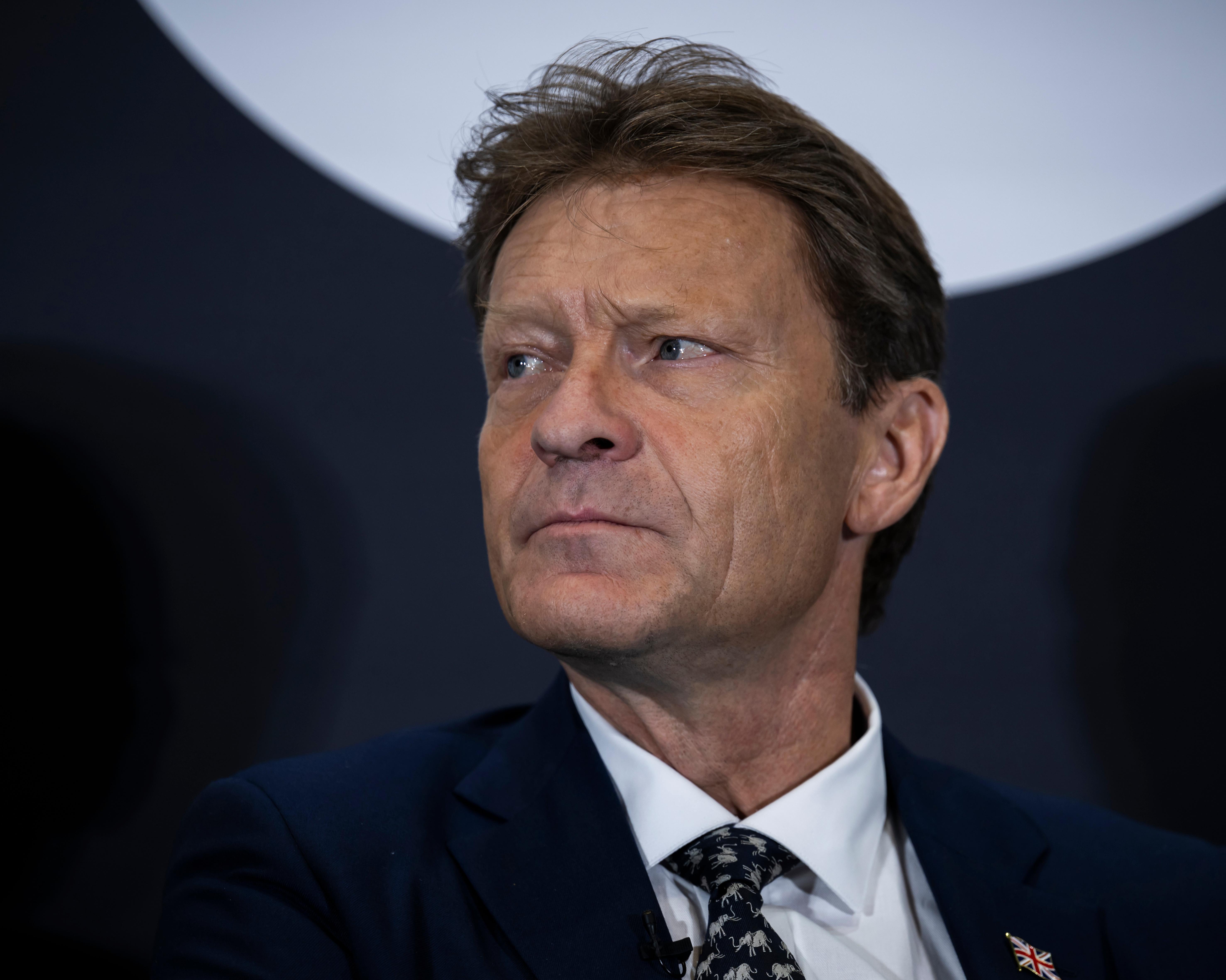 Close-up portrait of a suited man looking to one side against a dark backdrop.