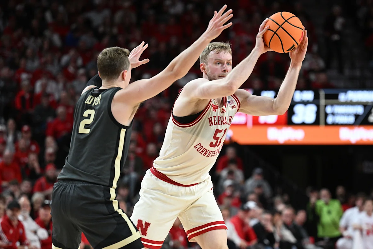 Basketball player in Nebraska uniform reaches for the ball against a defender.
