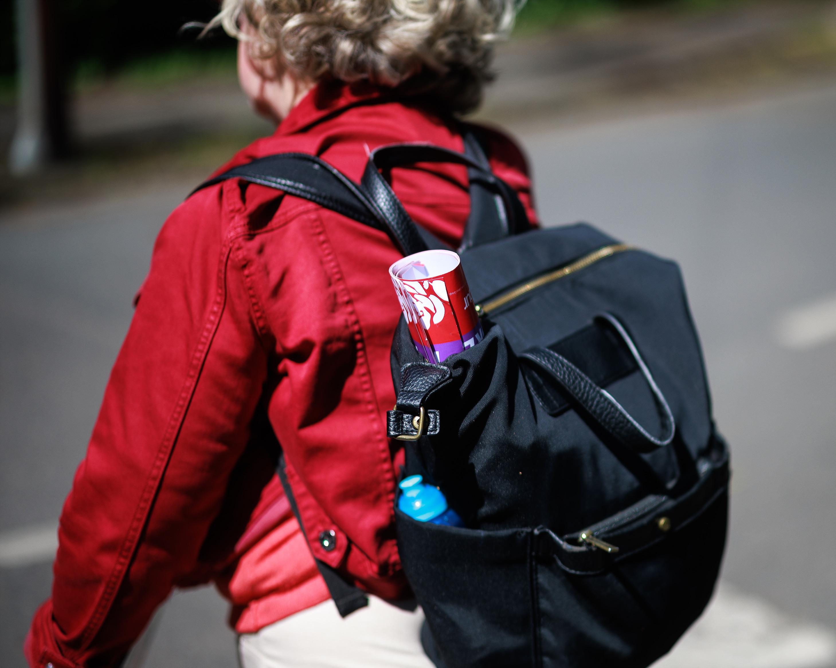 Person in a red coat carries a black backpack with a rolled-up poster.