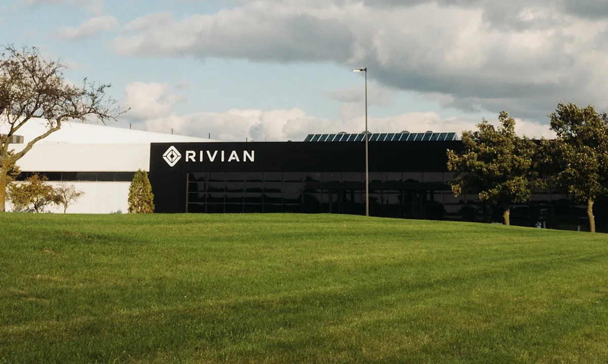 Rivian-branded modern building behind a broad green lawn beneath a cloudy sky