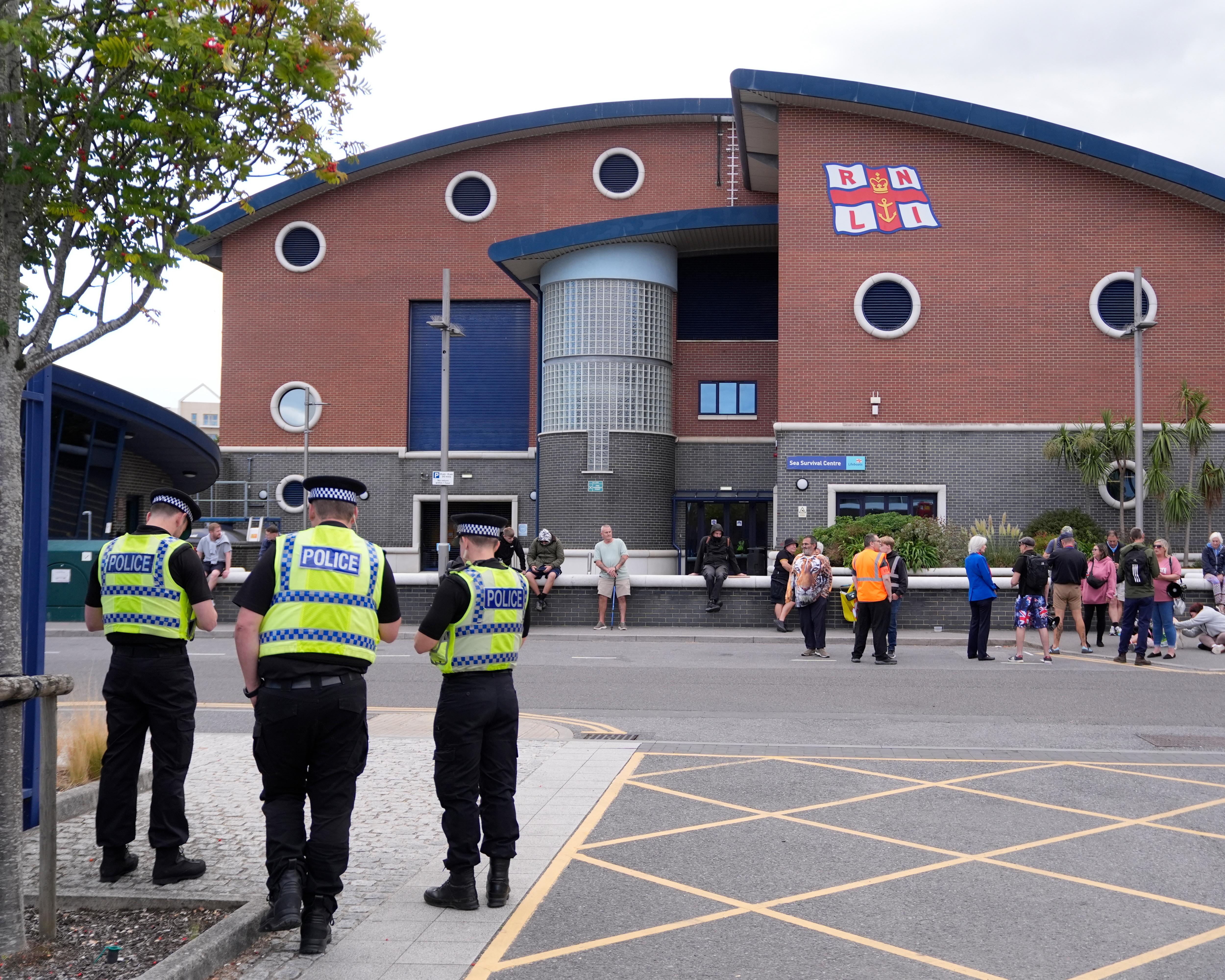 Police officers stand outside an RNLI building as people gather near its entrance.