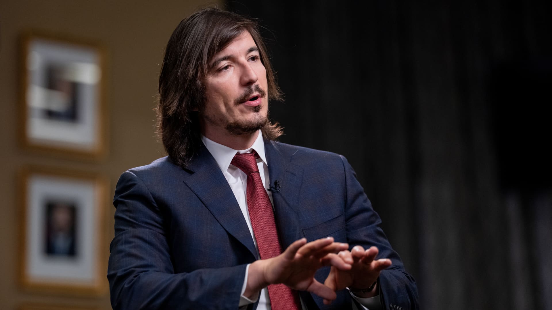 Suited man speaking and gesturing during an interview against a dark backdrop