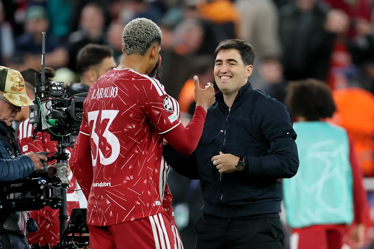 Liverpool player Ronald Araújo gestures while speaking with a smiling man beside a television camera