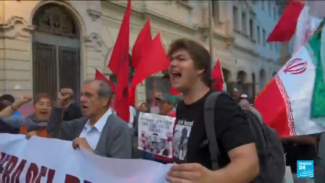 Protesters march with red flags and a large banner outside a historic building.