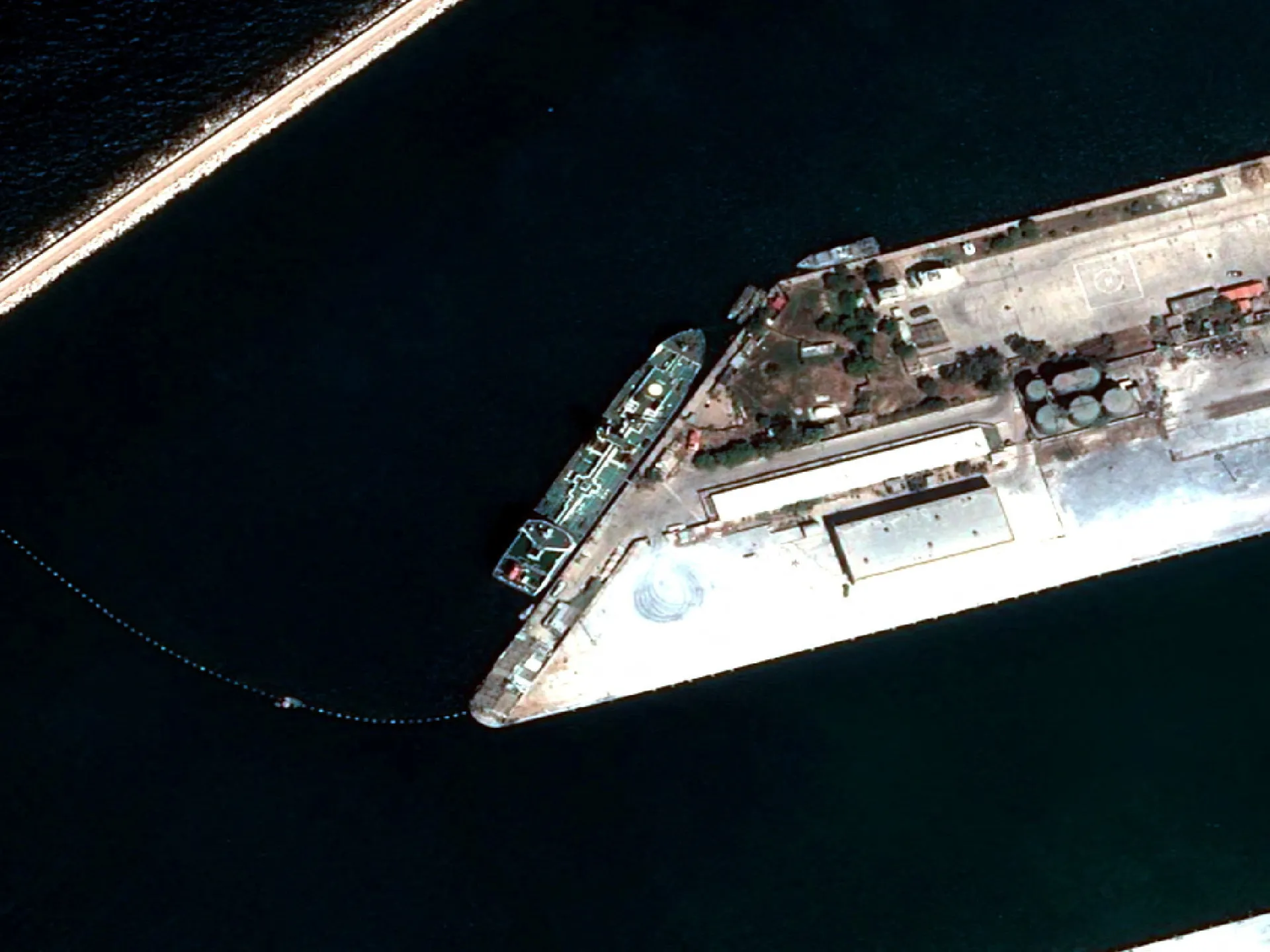 Aerial view of a large vessel moored beside a waterfront facility surrounded by dark water.