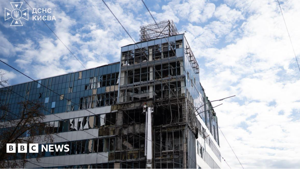 A damaged glass office building with shattered windows stands beneath a cloudy sky, with BBC News branding.