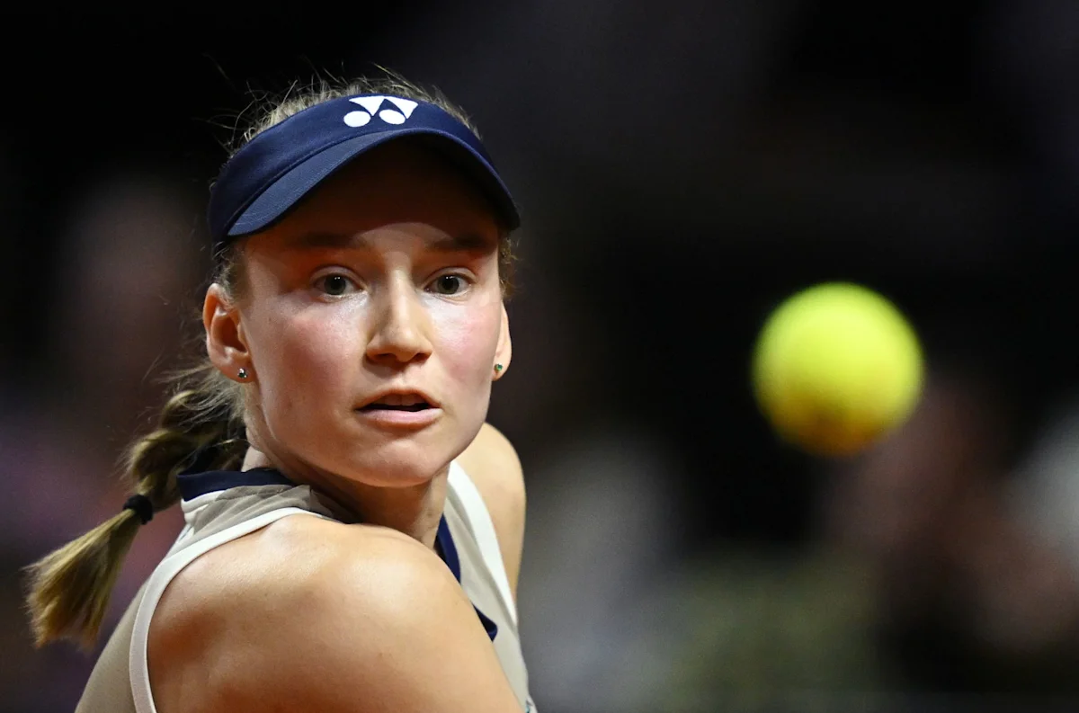 Female tennis player watches a yellow ball during a match, wearing a navy visor and white top
