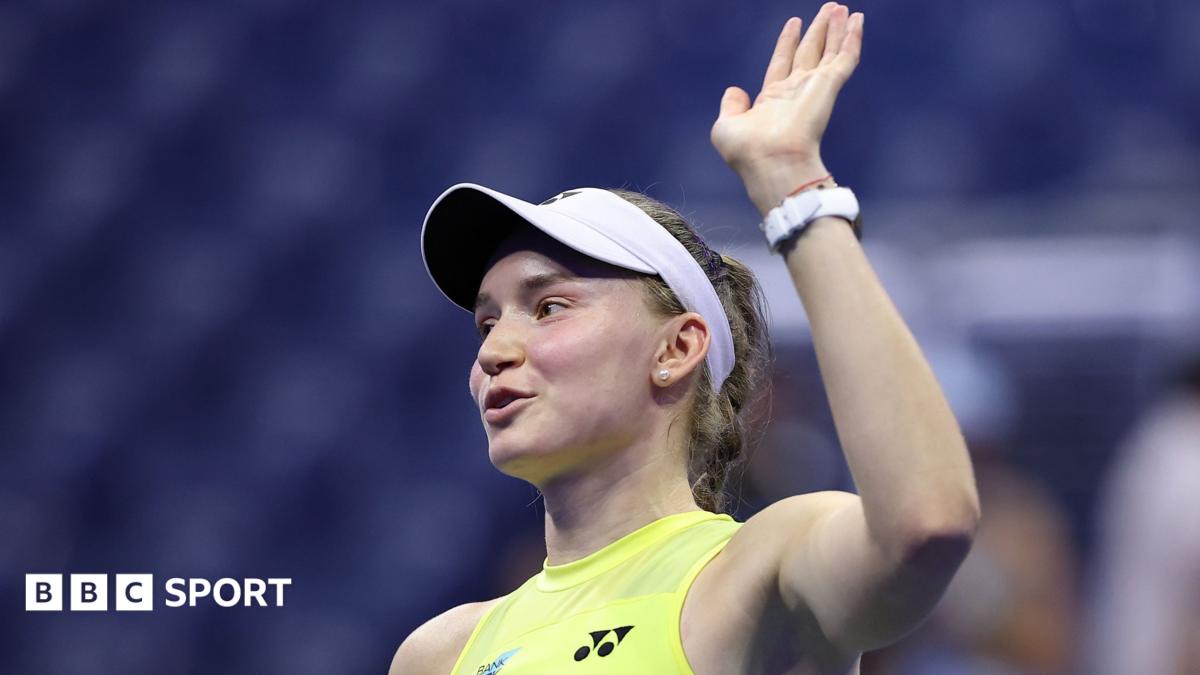 Tennis player in visor raises her hand while wearing a bright yellow shirt