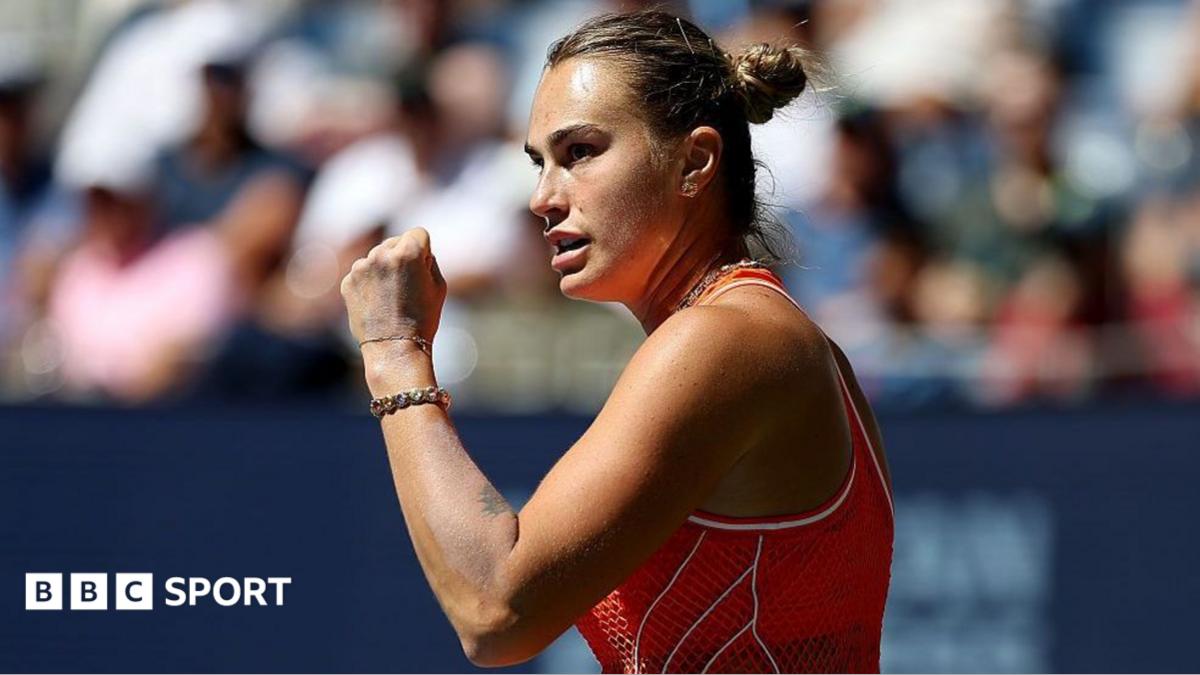 Tennis player in red raises a clenched fist during a match, with blurred spectators behind