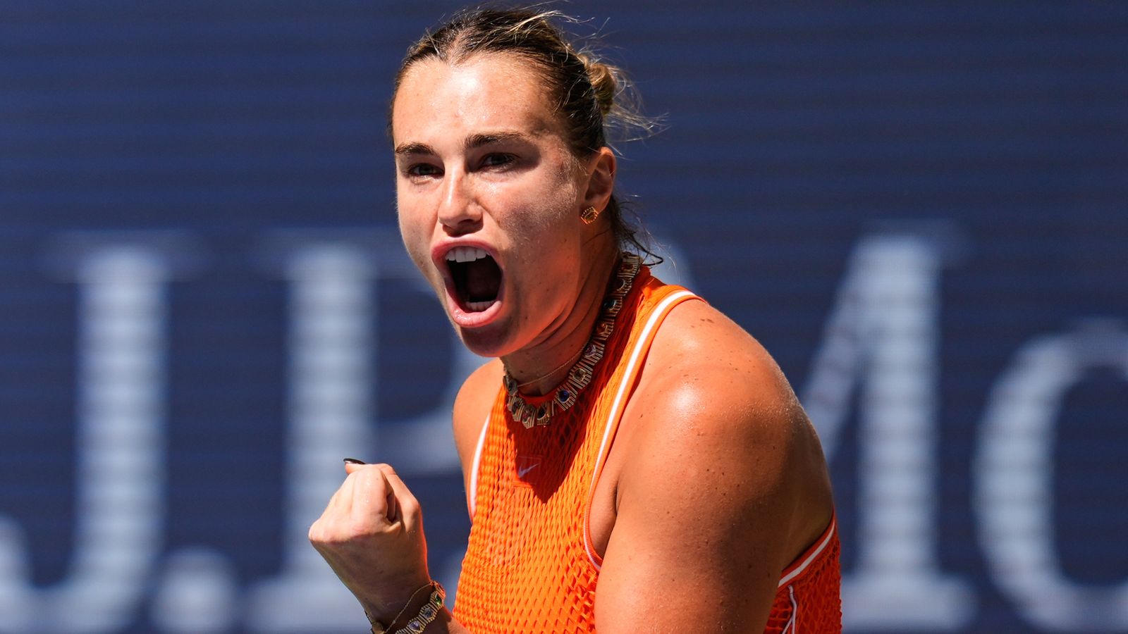 Tennis player in orange clenches her fist and shouts in celebration during a match