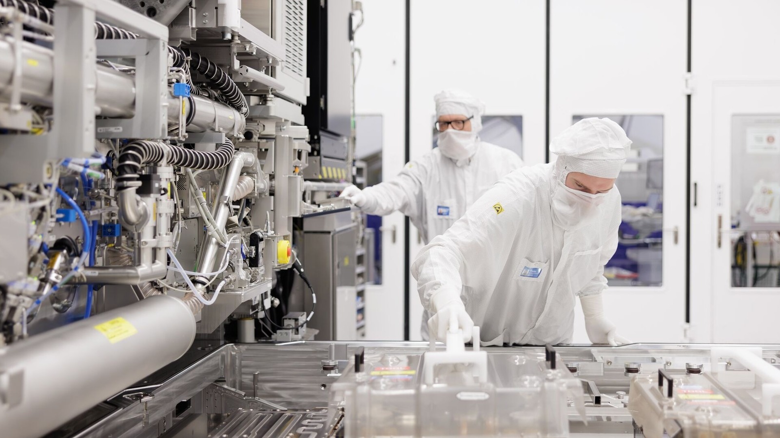Cleanroom workers operate advanced semiconductor manufacturing equipment inside a bright production facility.