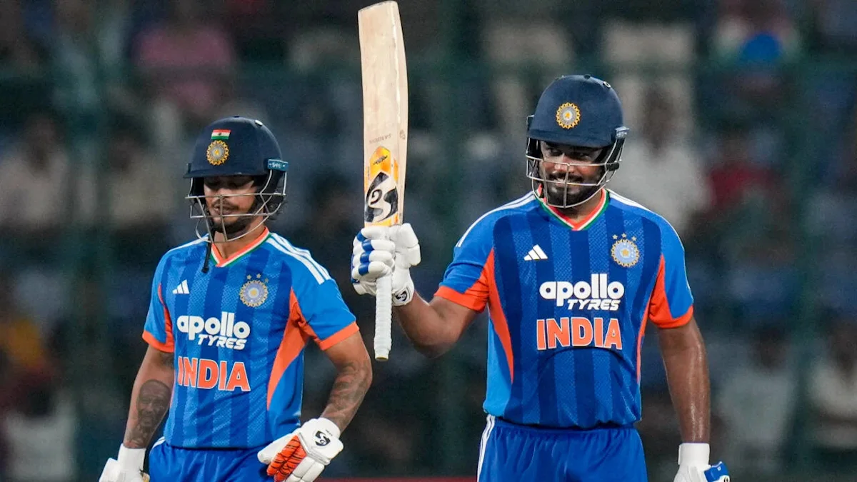Two Indian cricket batters in blue jerseys stand together, with one raising his bat.
