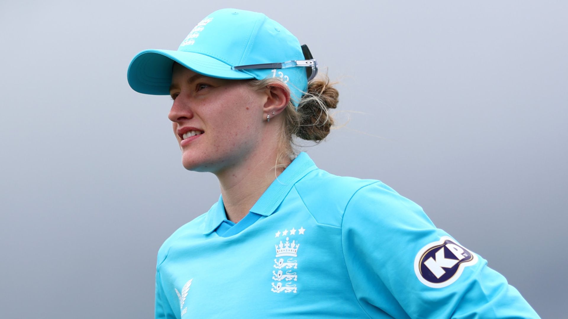 England women’s cricketer wearing a turquoise cap and shirt, shown in profile.