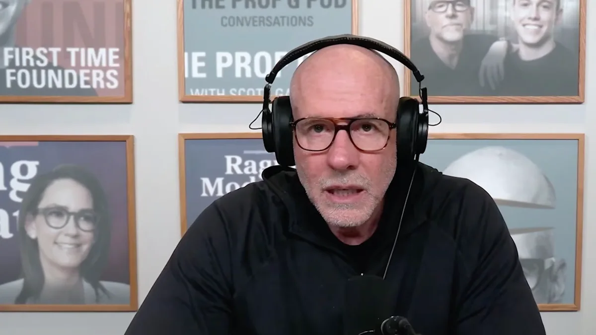 Bald man wearing glasses and headphones speaks into a microphone in front of framed posters.