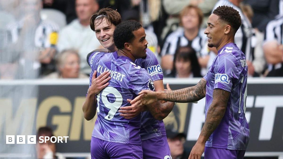 Four footballers in purple kits celebrate together during a match in front of spectators