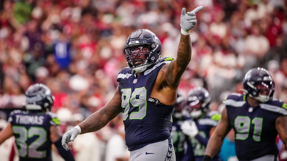 Seattle Seahawks player in navy number 99 uniform raises a gloved hand during a game.