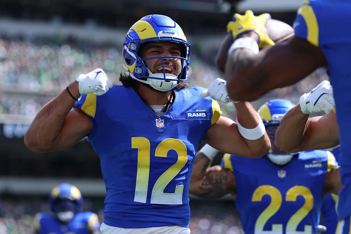 Football player wearing a blue and yellow Rams uniform raises both arms during a game