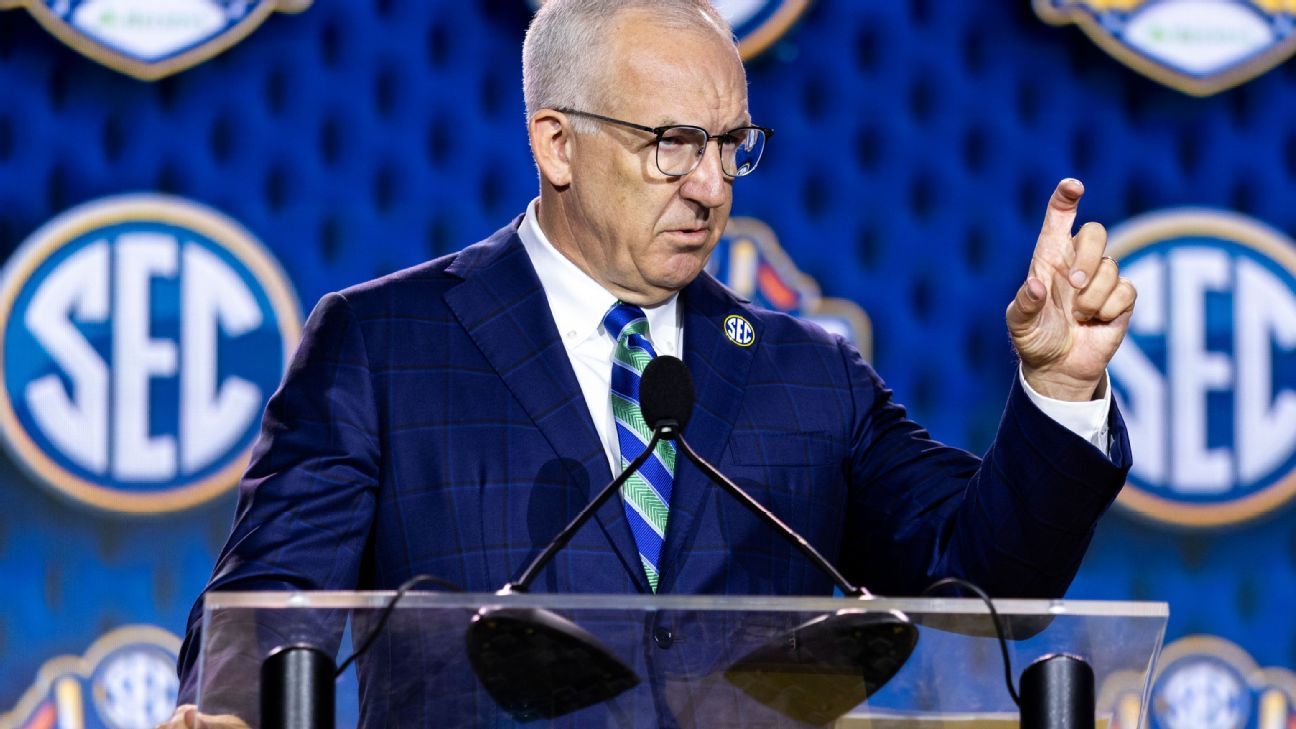 Man in suit and glasses gestures while speaking at a podium before SEC logos.