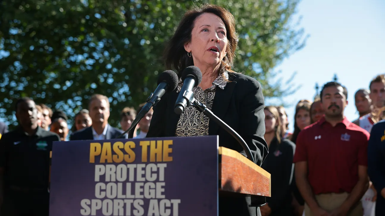 A woman speaks at an outdoor podium marked “Pass the Protect College Sports Act,” with people gathered behind her.