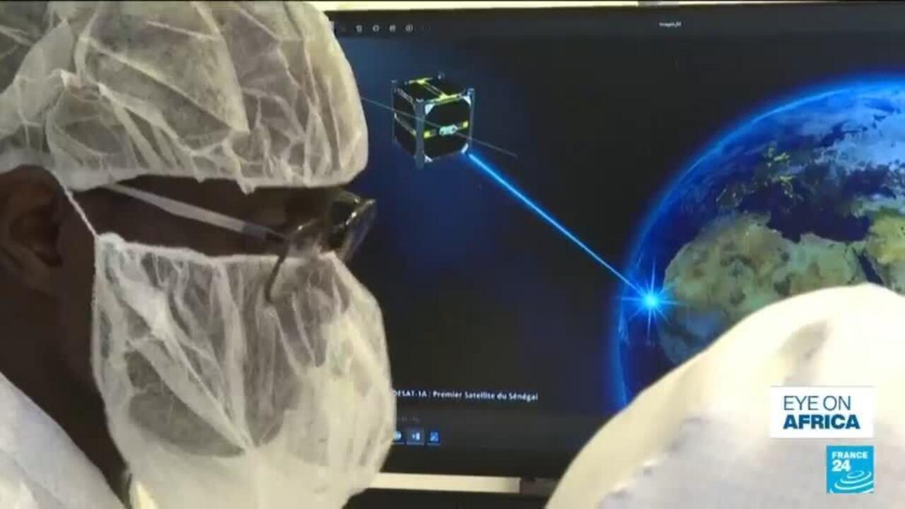 Two people in protective hairnets and glasses view a satellite tracking display beside a globe.