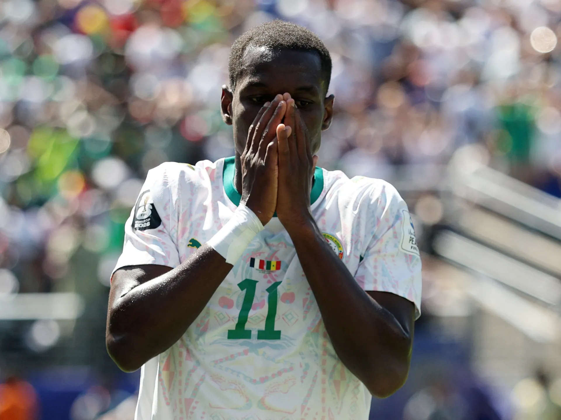 A Senegal player in a white number 11 jersey presses his hands to his face on the pitch.