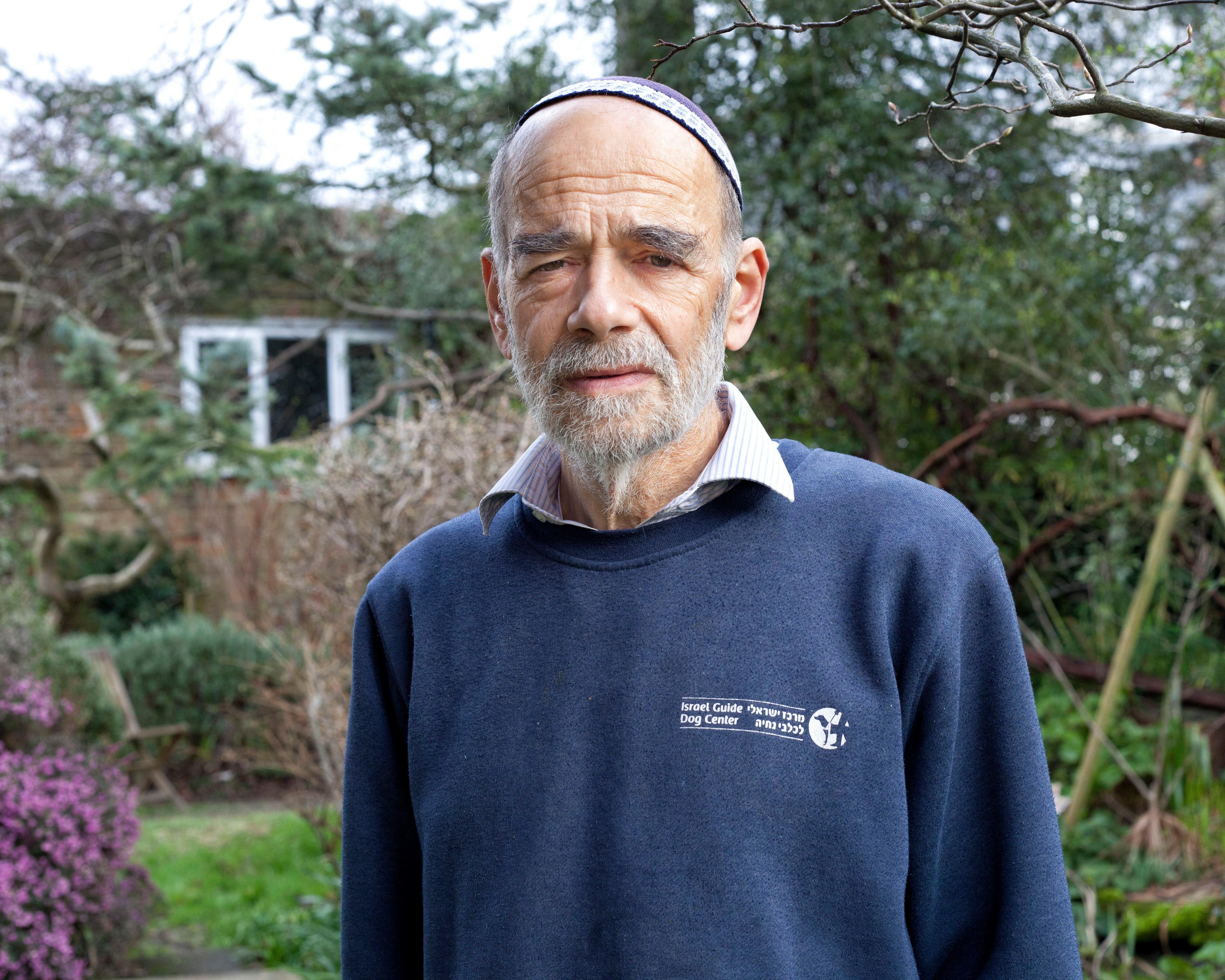 Bearded man wearing a kippah and navy sweater standing outdoors among trees