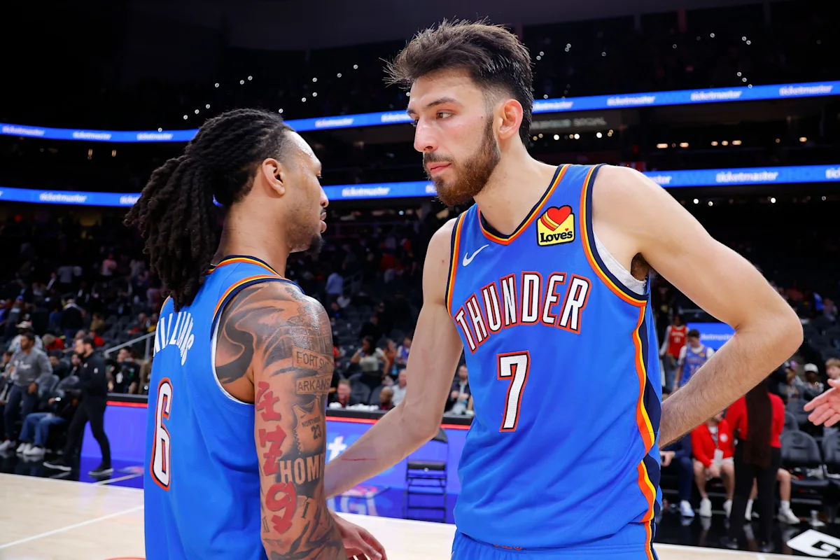 Two Oklahoma City Thunder players talk courtside in blue basketball uniforms during an arena session.