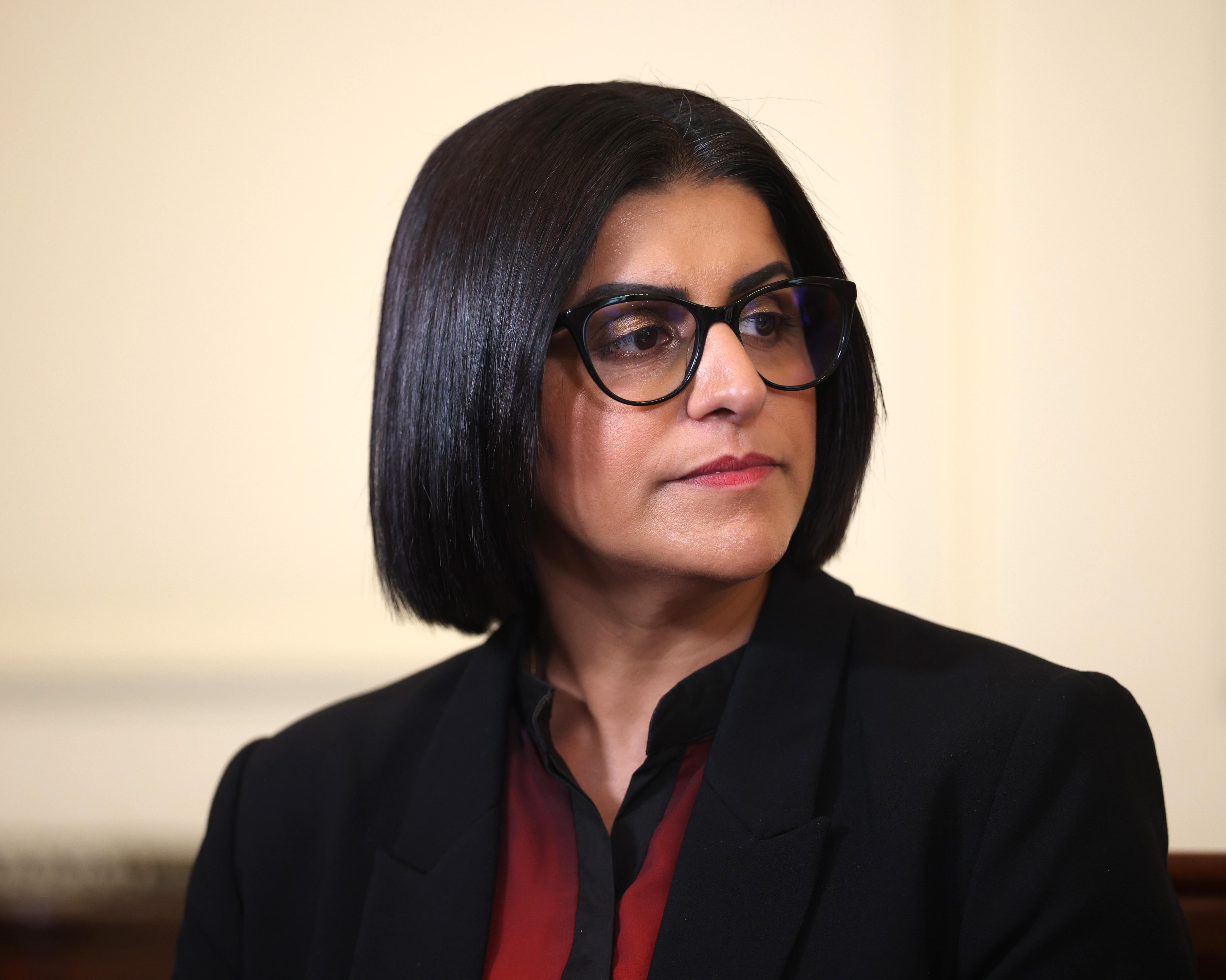 Woman with dark bobbed hair and glasses wearing a black jacket, photographed in close-up.