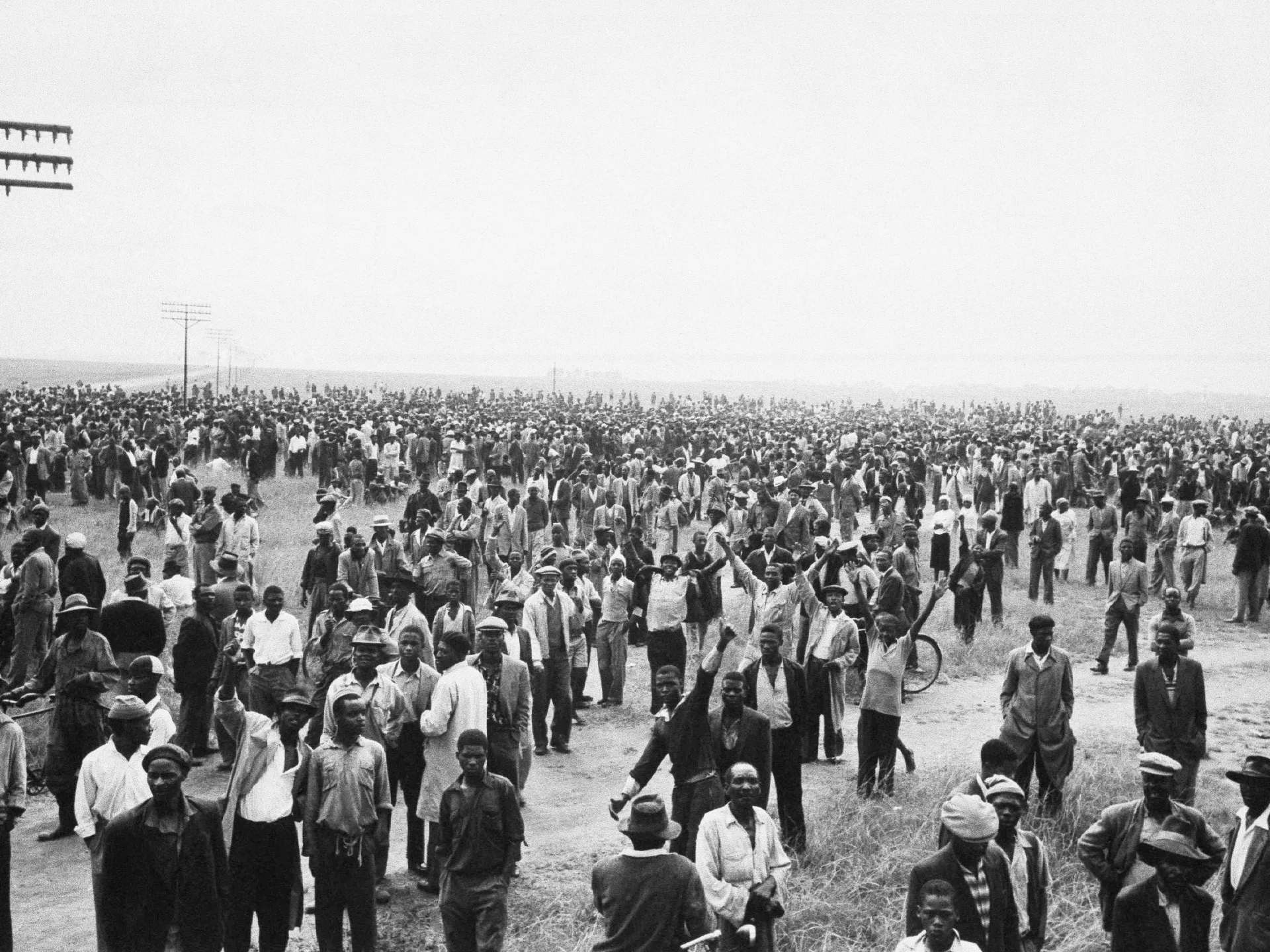Large crowd of Black people gathered in an open field, with utility poles visible in the background.