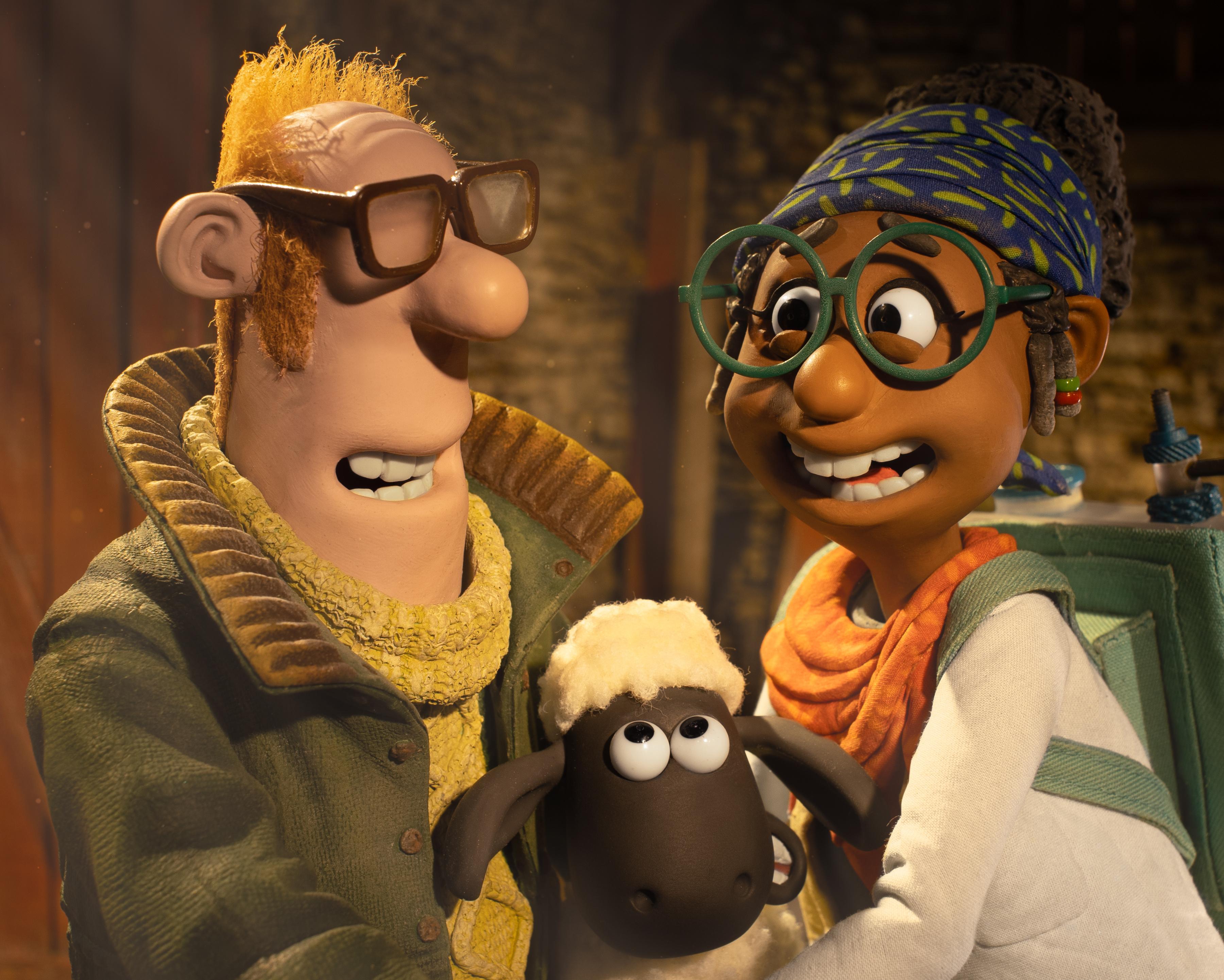Two claymation characters wearing glasses pose with Shaun the Sheep in a warmly lit scene.