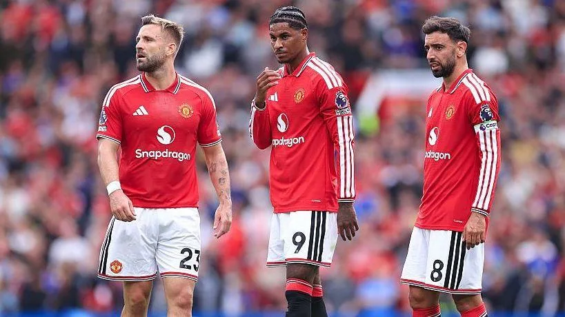 Three Manchester United players in red shirts stand on the pitch during a match