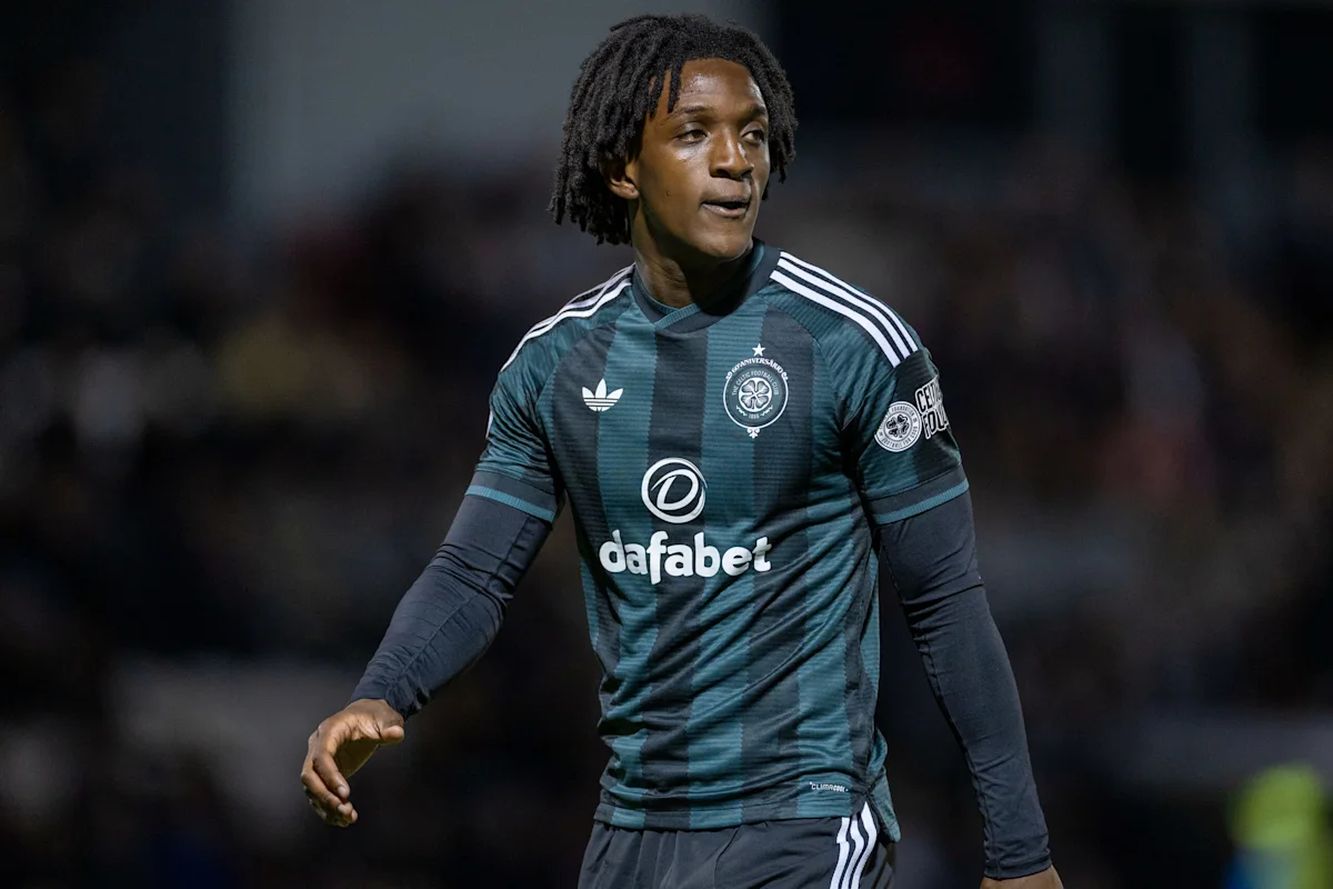 Footballer in Celtic kit with dreadlocks stands on pitch during a match.