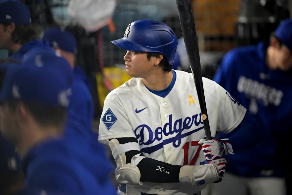 Baseball player in Dodgers uniform and helmet holding a bat in the dugout
