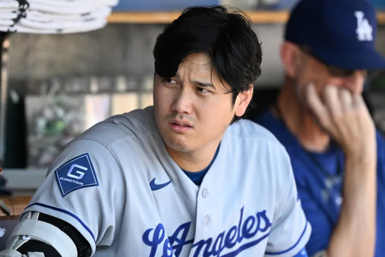 Baseball player in a Dodgers jersey sits in the dugout with a concerned expression