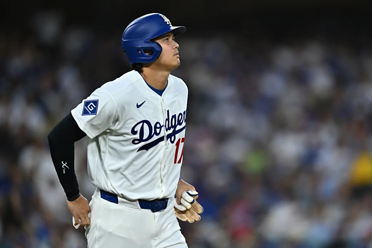 Baseball player in a Dodgers uniform and helmet stands on the field, looking upward.
