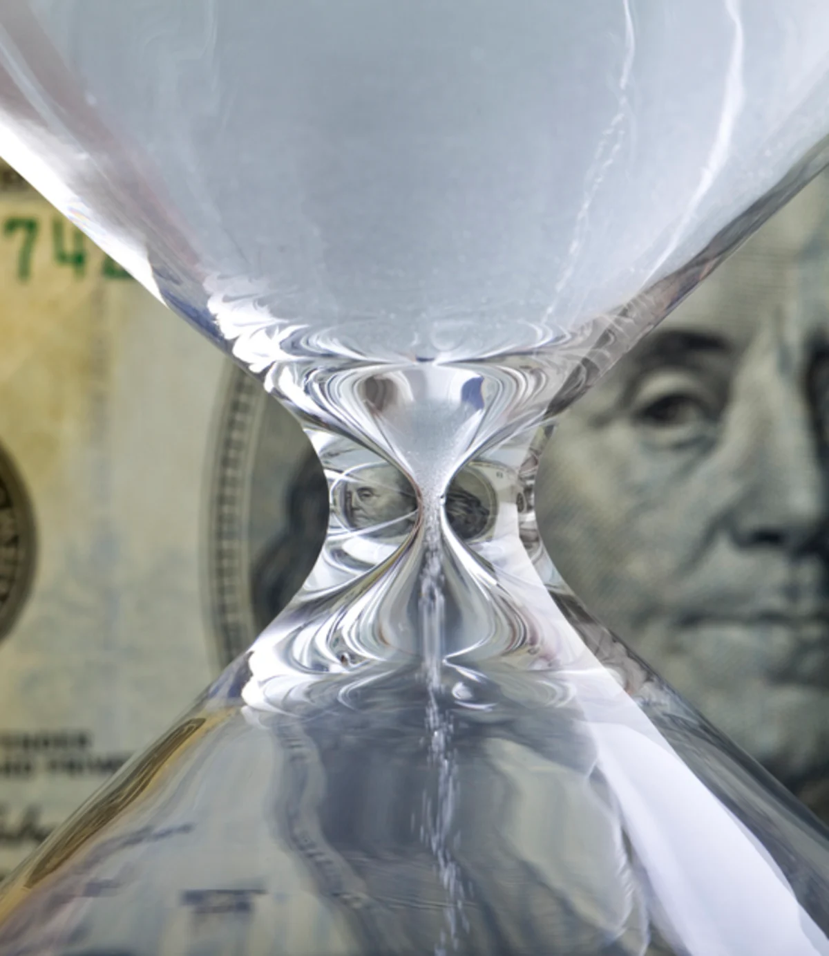 Hourglass containing dollar bills, with Benjamin Franklin visible through the glass.