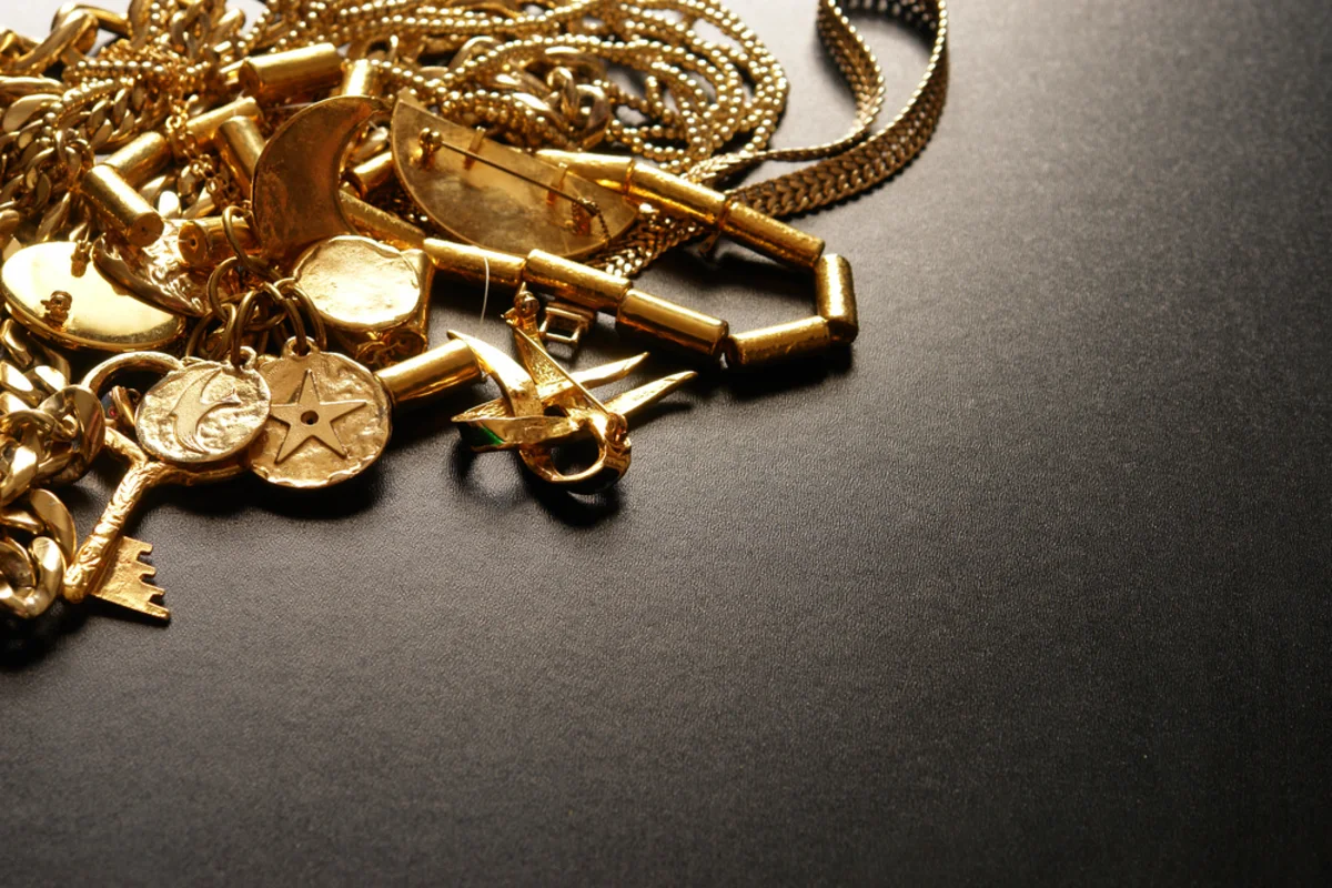 Assorted gold jewelry, chains, coins, charms, and a key arranged on a dark surface.