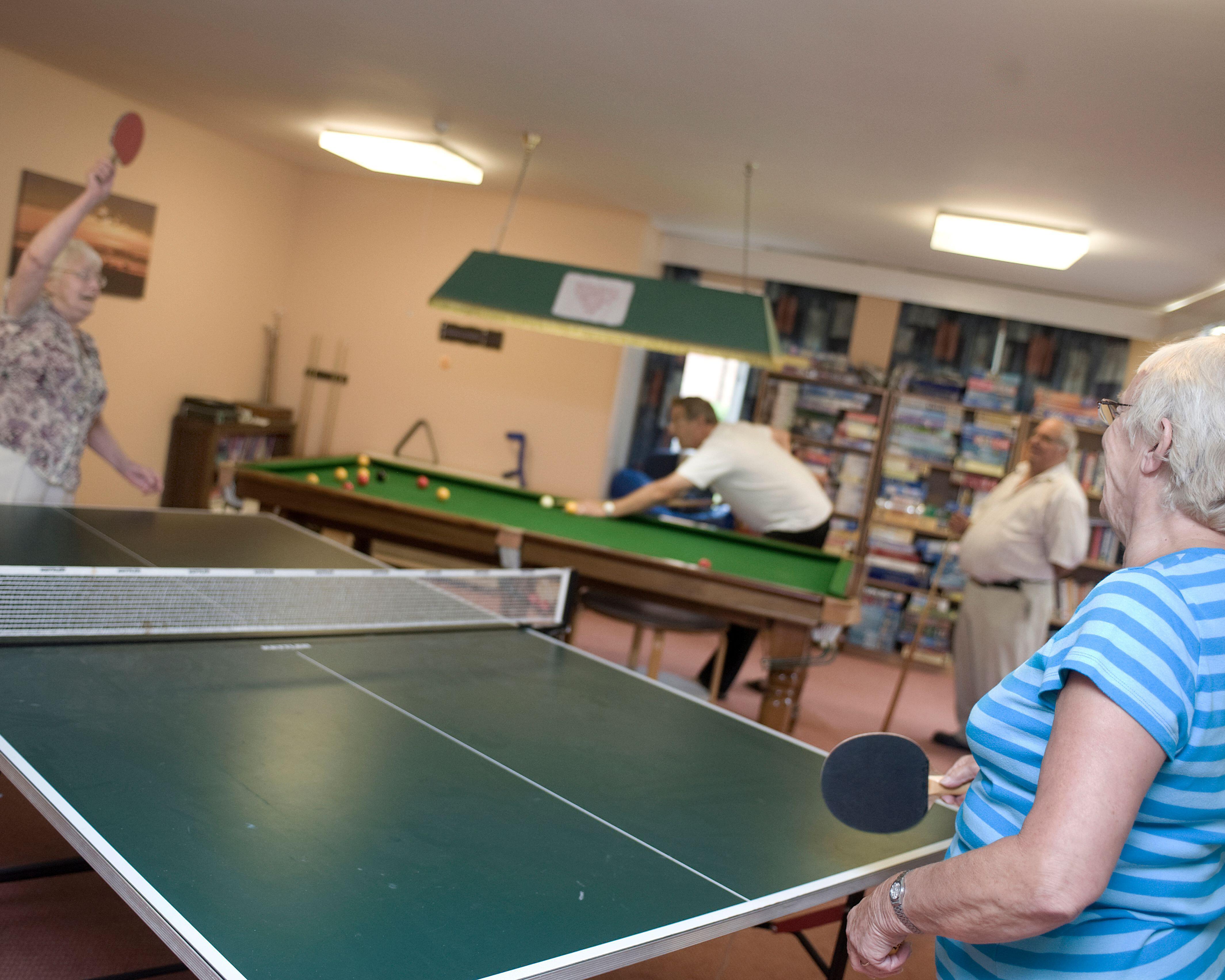 Older adults play table tennis and billiards in a community recreation room.
