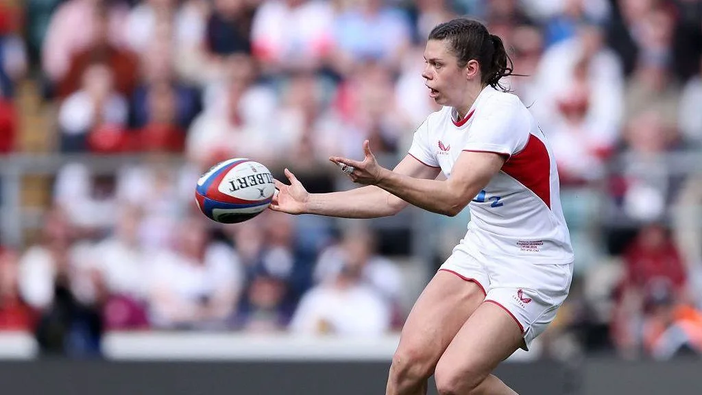 Rugby player in white and red kit reaching to catch a ball during a match