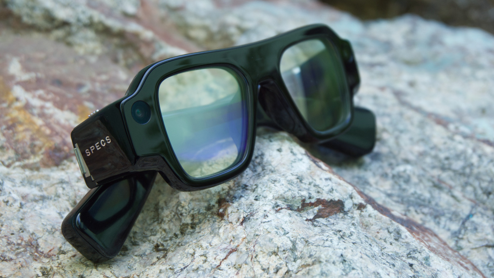 Black smart glasses with visible camera lenses resting on a textured stone surface