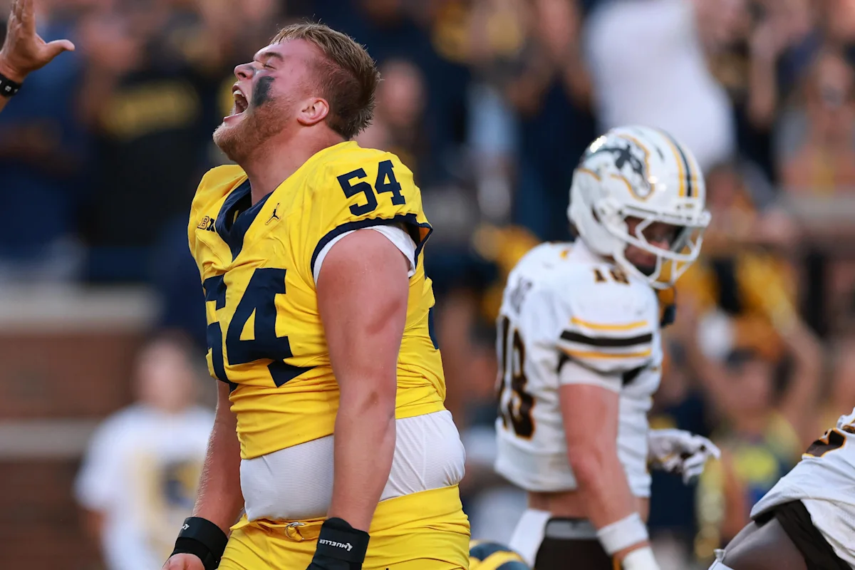 Michigan football player No. 74 celebrates as Western Michigan players stand nearby during a game.
