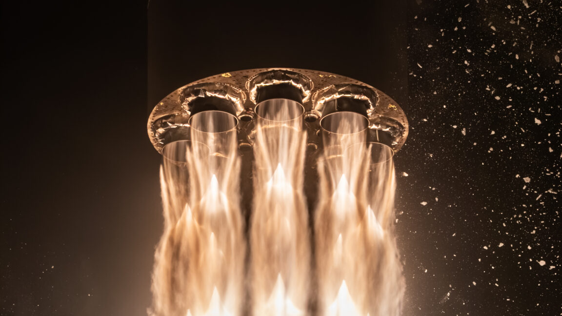 Close-up of rocket engine nozzles producing bright orange exhaust against a dark background