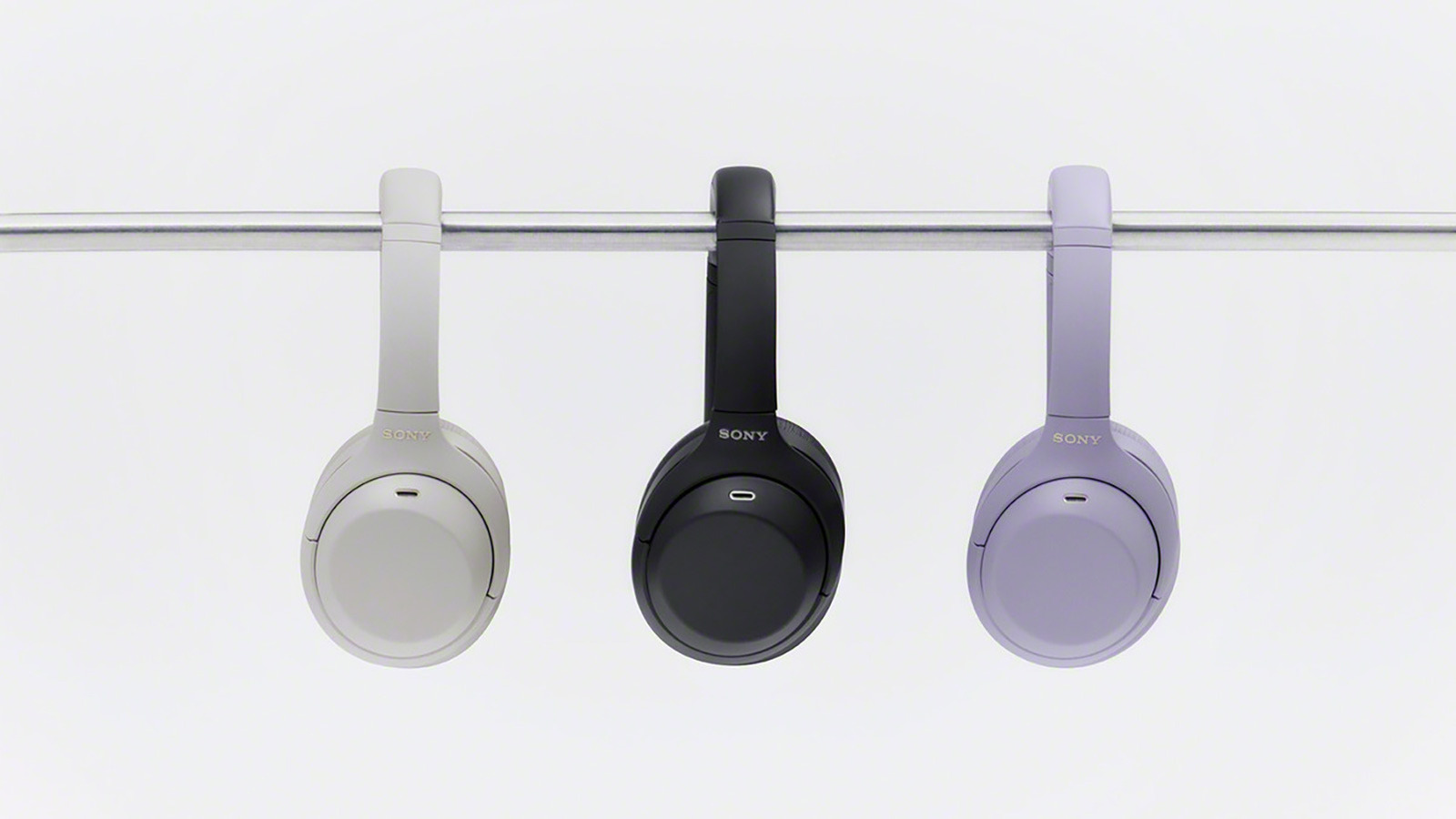 Three Sony over-ear headphones in white, black, and lavender hang from a horizontal rail.