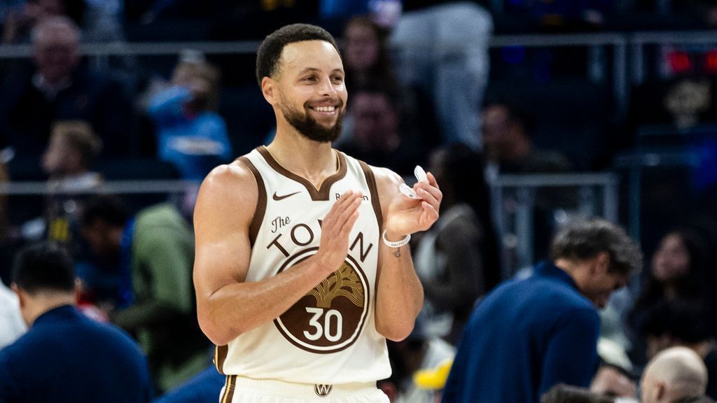 A basketball player wearing a white number 30 jersey smiles and claps on the court.