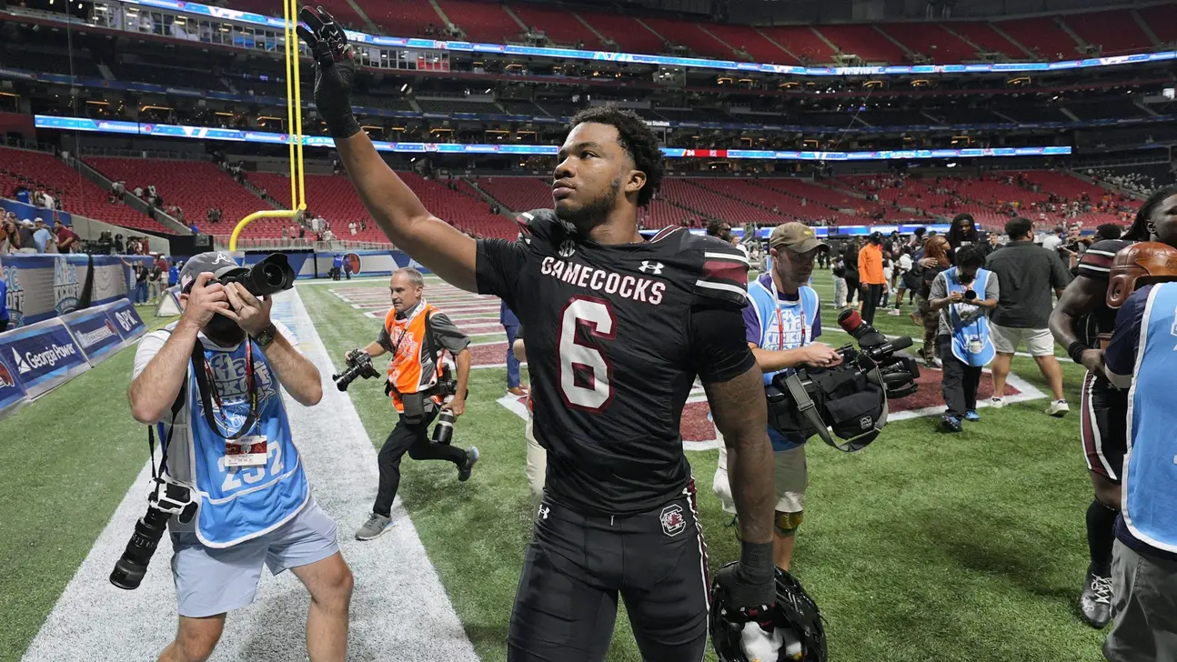 South Carolina player in a black number 6 uniform raises his hand on the field among photographers.